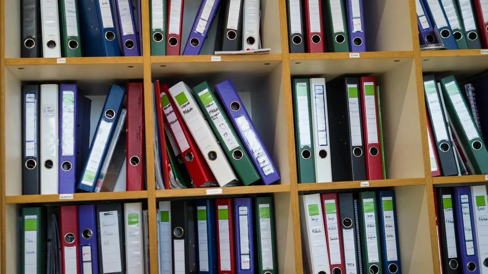 Wooden office shelves filled with rows of coloured ring binders with handwritten spine labels
