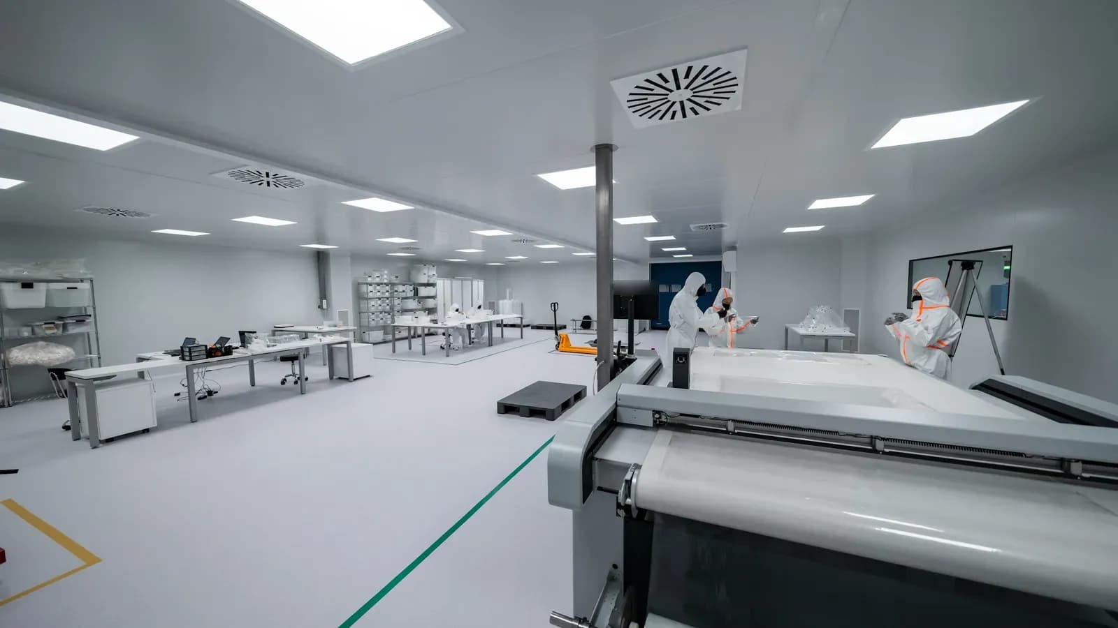 Cleanroom operators in white coveralls working at benches and machinery in a production area