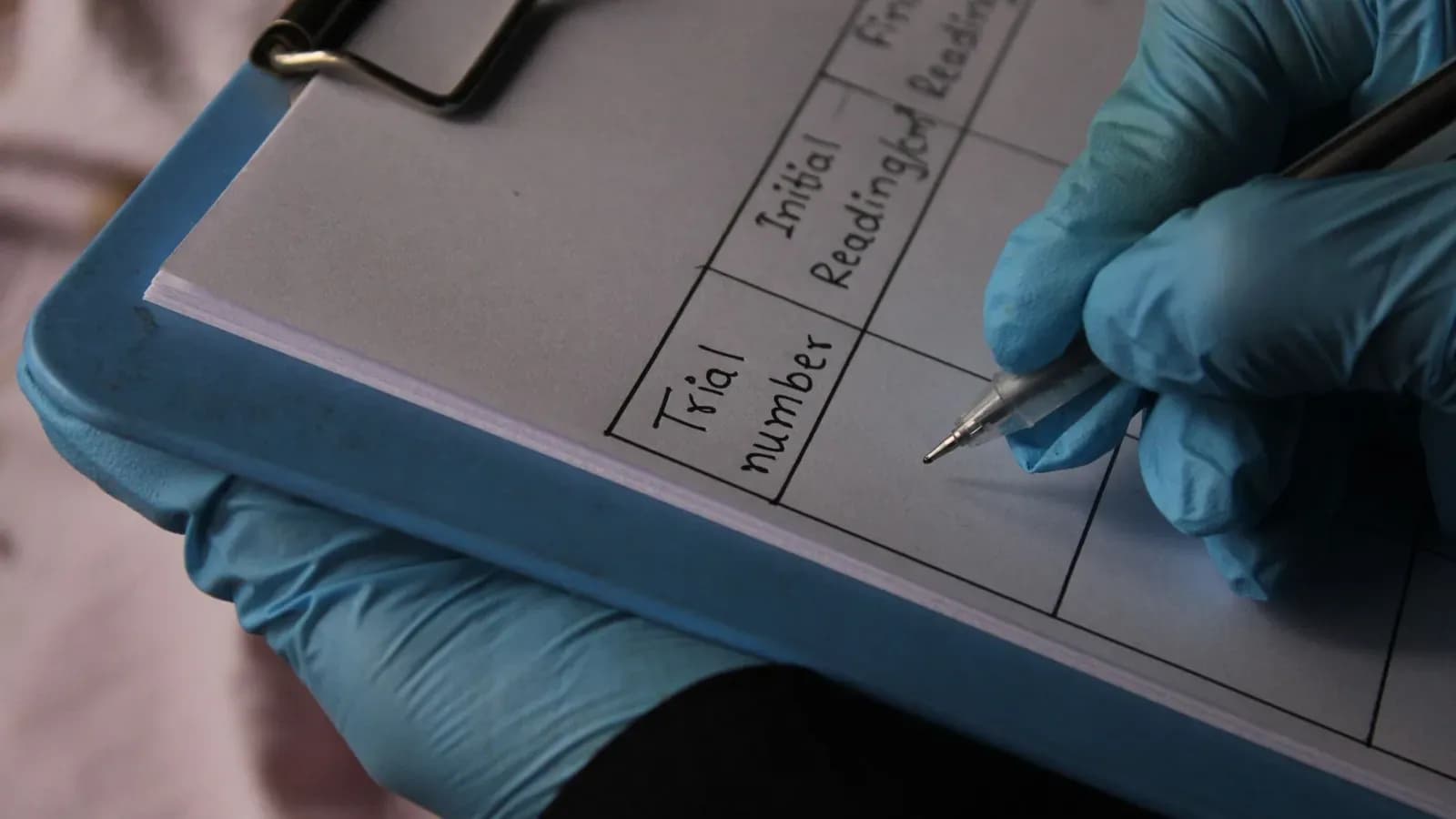 Gloved hand writing with a pen on a pre-printed data sheet clipped to a clipboard