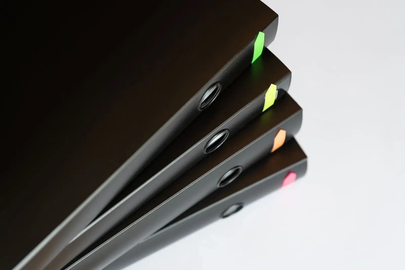 Four black ring binders with coloured index tabs stacked at an angle on a white surface