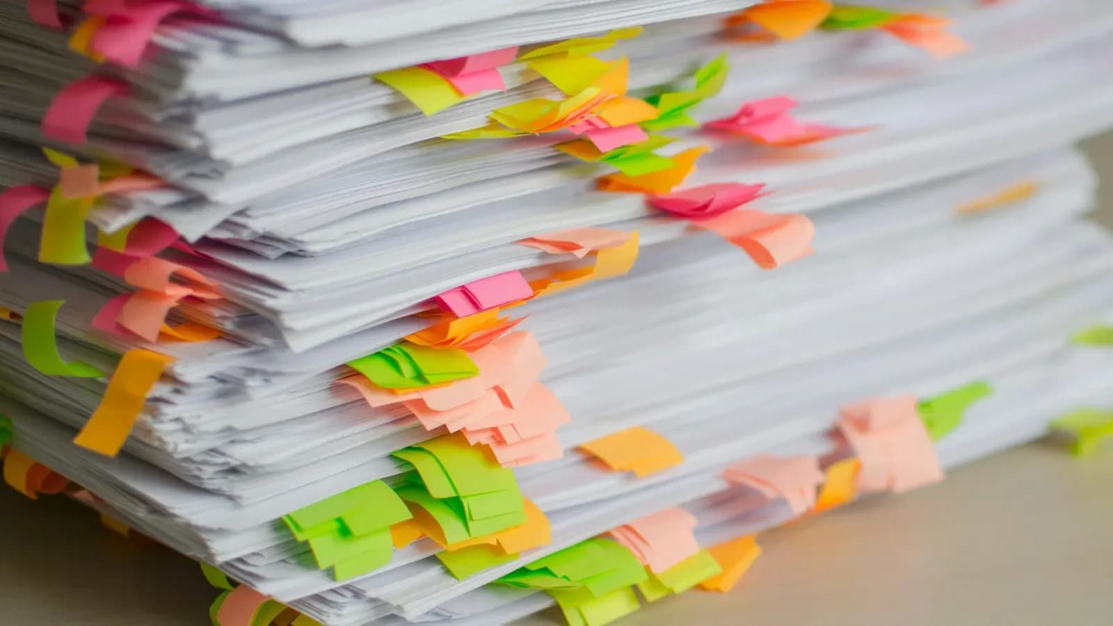 A tall stack of printed documents with many pink, orange, yellow and green sticky tabs marking pages